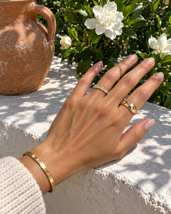 Hand on a garden wall wearing gold rings and a gold bangle