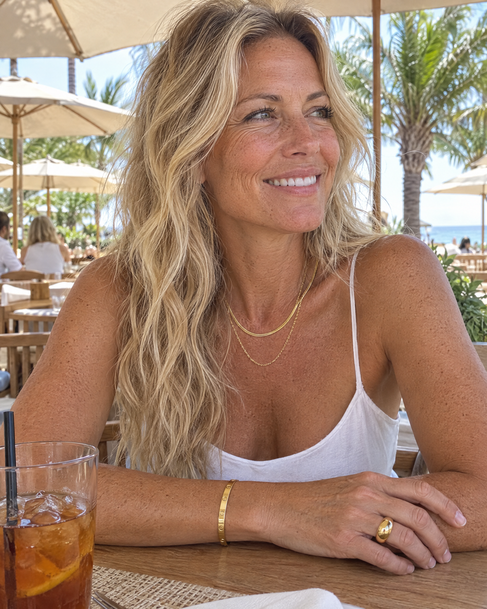Woman at a beach club wearing a layered gold necklace, bangle and ring